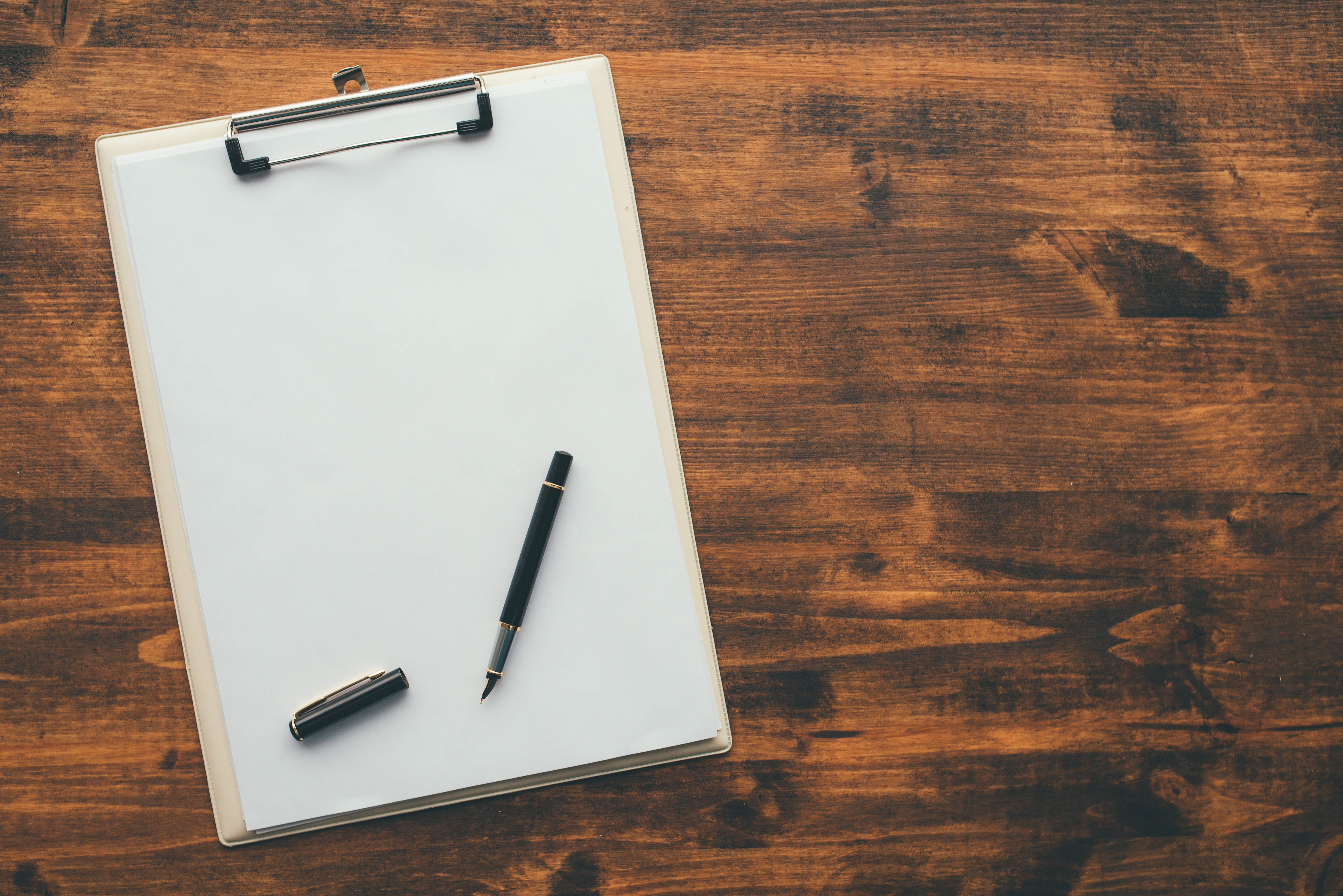 Overhead view of blank clipboard note pad paper with pen on office table as mock up copy space for check or to do list