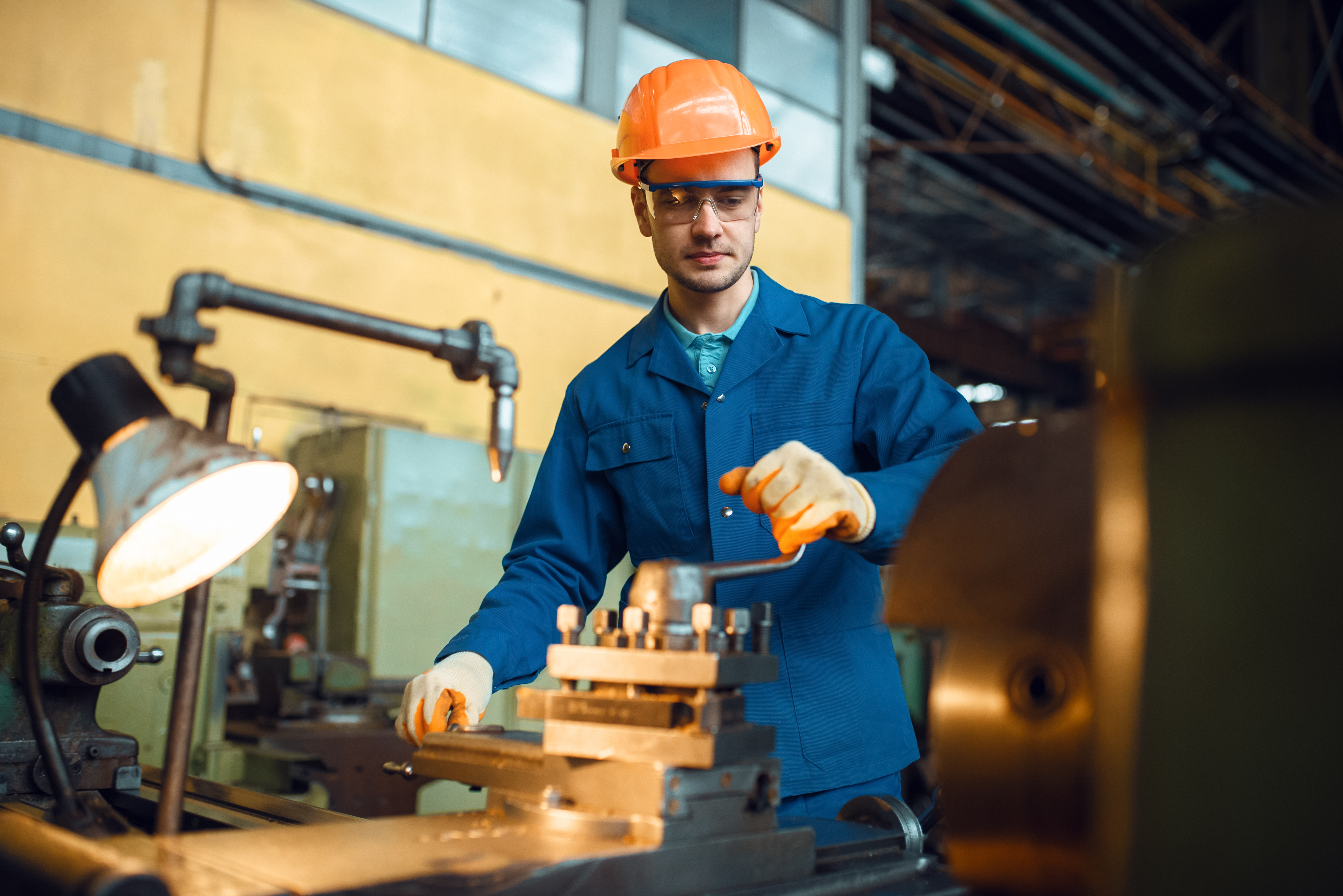 Worker in uniform and helmet works on lathe, factory. Industrial production, metalwork engineering, manufacturing